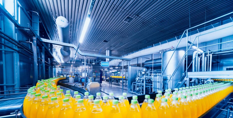 Dozens of juice-filled bottles line a conveyor system inside of food and beverage processing facility